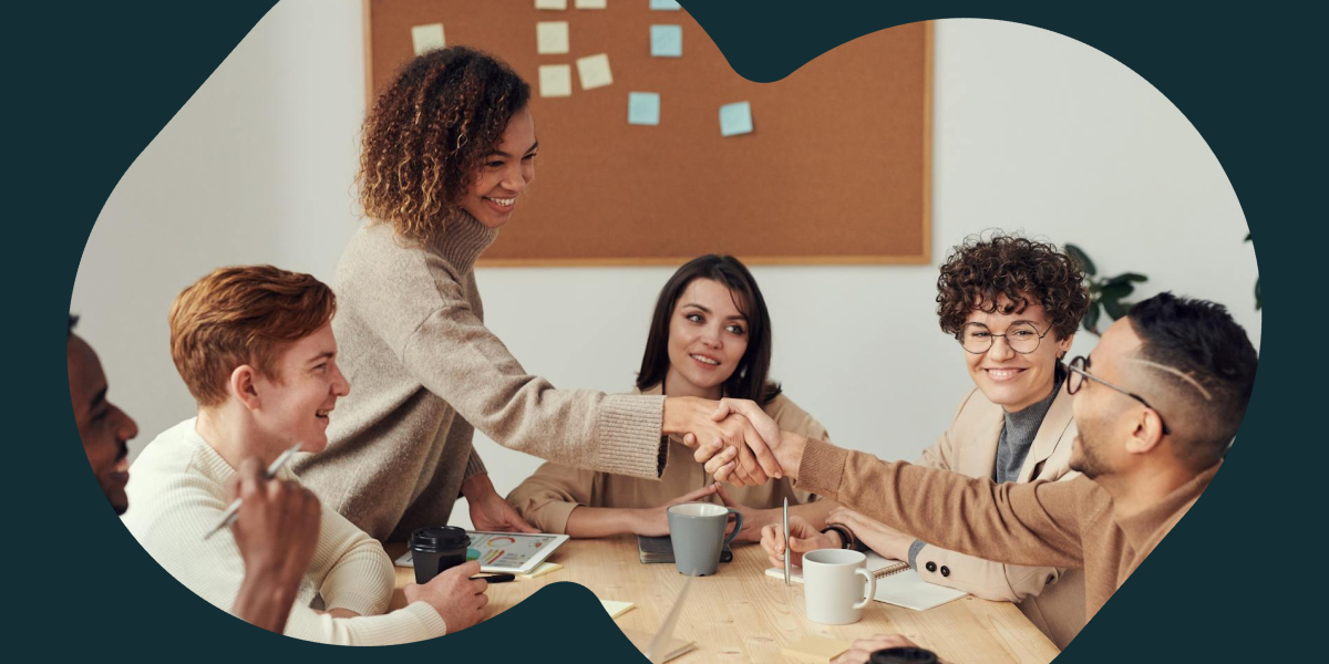 A team of workers sit around a table smiling and shaking hands